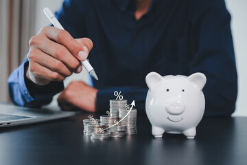 Businessman hand putting a coin into a white piggy bank for saving money concept.