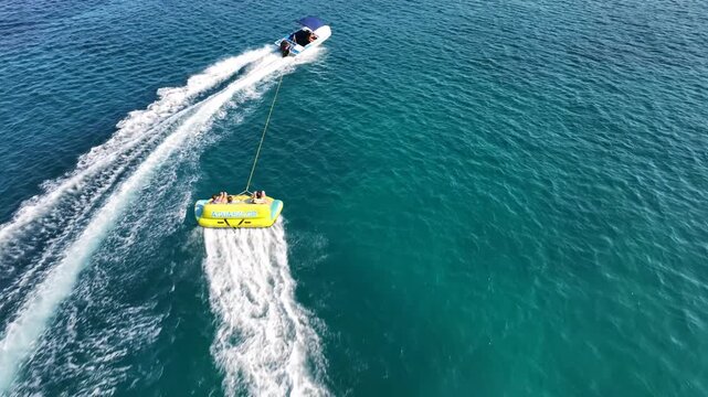 Aerial drone cinematic tracking video of inflatable donut towed by power boat a fun water sport activity in deep blue open ocean sea