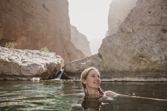 Woman swims in Wadi in bottom of deep canyon in Oman