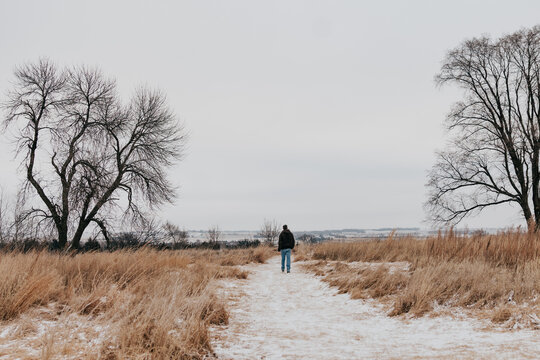 Adult male walks along snow covered path through field of golden grass