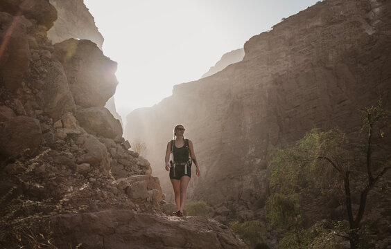 Woman hikes through deep canyon wadi at sunset in Oman