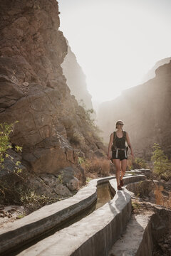 Female hiker walks along irrigation canal in desert canyon, Oman