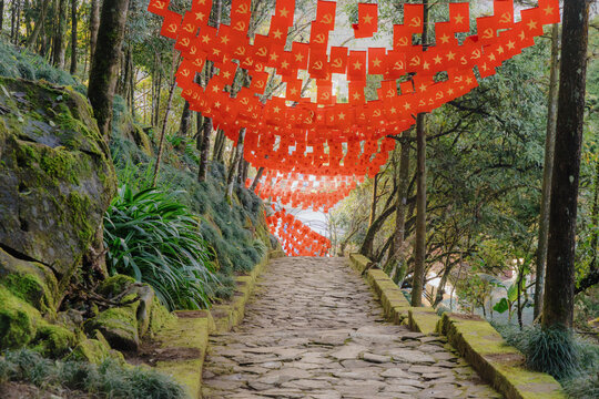 A tourist walks along a stone path decorated with communist flags in Ham Rong Park, Sa Pa, Lao Cai, Vietnam. The flags create a festive atmosphere for visitors.