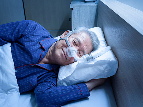 An elderly Asian man is sleeping peacefully while wearing a CPAP machine, improving his sleep health.
