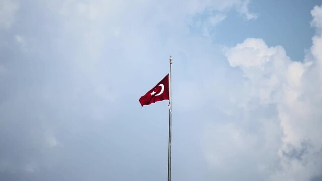 Turkish flag with white crescent moon and star on red background fluttering majestically on flagpole under cloudy sky. Symbol of national identity and sovereignty. Slow motion x4