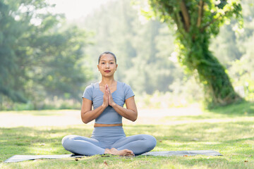 Fototapeta premium Asian woman yoga meditation sitting outdoor park scene shows calm focus during early morning practice on grass under soft natural light surrounded by green tree background