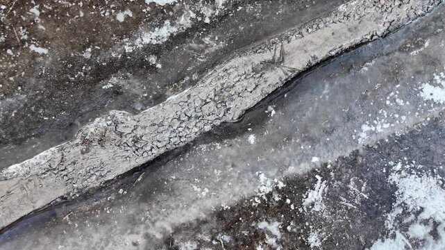 Early spring thaw on a frozen road. Footprints and tracks mark the slippery, melting ice.