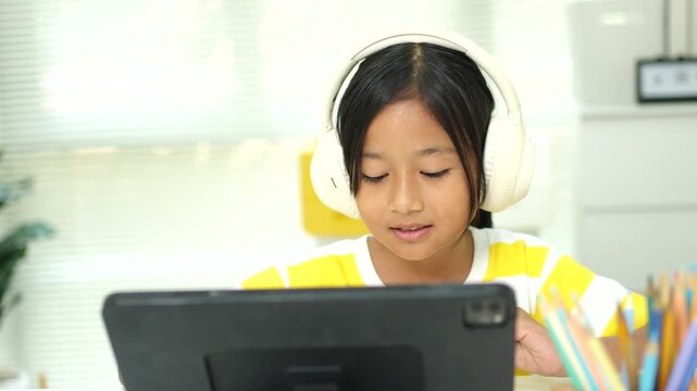 Asian girl with headphones enjoying online class on digital tablet