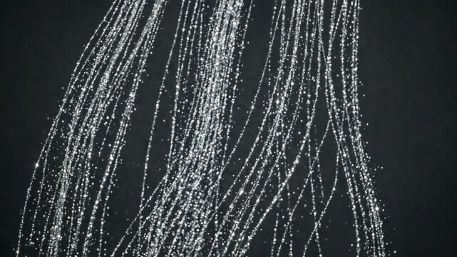 Macro shot of clear water streams falling in lines against a dark background with sparkling light reflections