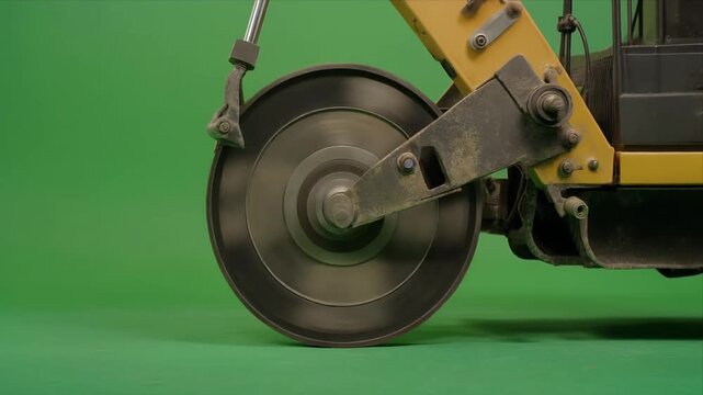 Rotating cutoff saw blade on construction machine against green screen.