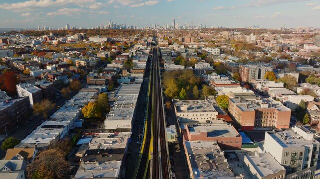 Aerial drone view of elevated train tracks running through a Brooklyn neighborhood with city skyline in the distance and autumn trees, filmed in ProRes 422HQ.
