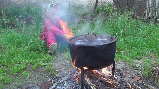 Child by Fire, Cooking at Fireplace in a Pot for Eating, Rustic Kid, Girl in Yard, Countryside