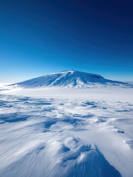 Isolated snow-capped mountain with smooth snowdrifts under clear blue sky in arctic landscape  