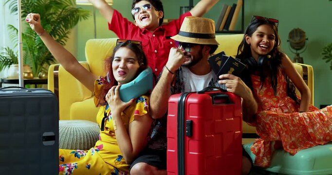 Cheerful young Indian family of four sitting together with suitcases, happily showing passports to the camera. Excitement for international travel, foreign holiday, and family vacation.
