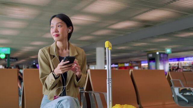 Asian woman starts her morning routine at the airport gate, listening to a podcast on her phone while waiting for departure. Concept of journey and solo travel.