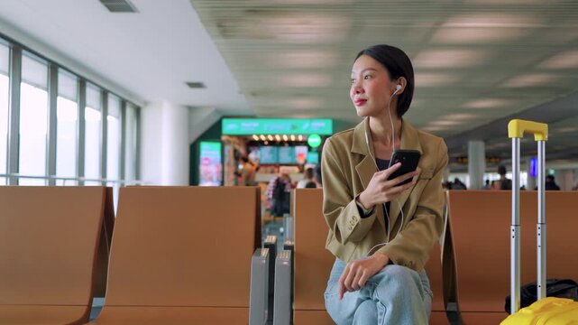 Asian woman starts her morning routine at the airport gate, listening to a podcast on her phone while waiting for departure. Concept of journey and solo travel. 
