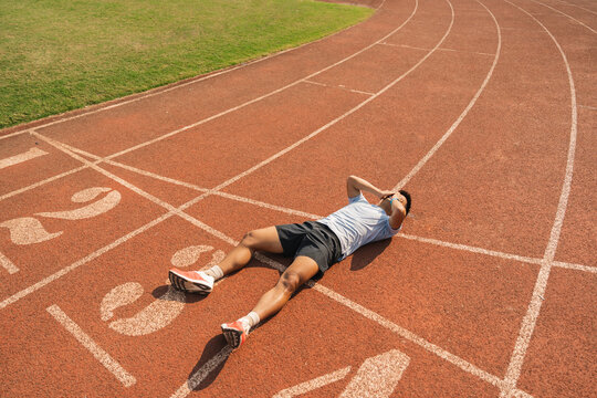 Athlete lies on track hands behind head resting after exercise Outdoor sports activity