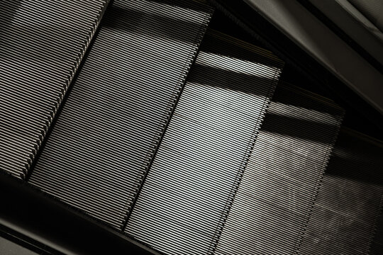 Close-up of escalator steps forming strong diagonal lines and repetitive metallic texture, creating an abstract pattern with light and shadow contrast
