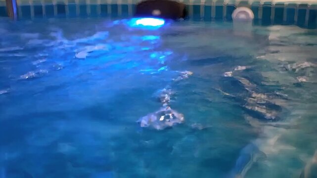 Close-up of gentle water ripples forming in a spa plunge tub. Blue underwater LED lighting illuminating bubbles in a jacuzzi pool. Hydrotherapy and wellness concept