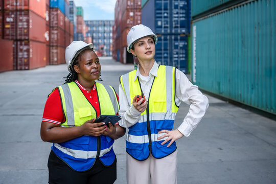 Female industrial workers engineer inspecting shipping container logistics with safety gear and radio communication