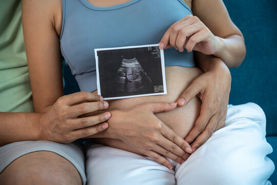 Asian expecting parents sharing a tender moment with baby ultrasound, pregnancy and love at home