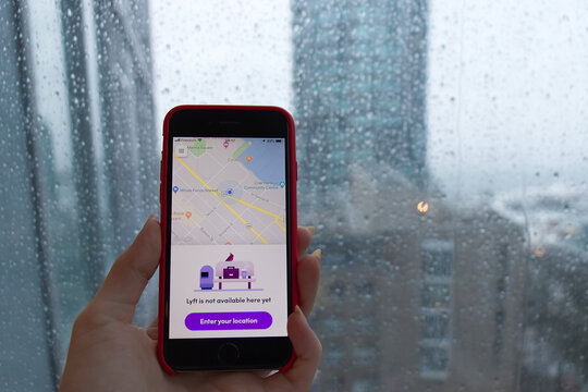 Hand holding a red iPhone displaying Lyft app unavailability message over a rainy window