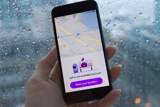 Hand holding a red iPhone displaying Lyft app unavailability message over a rainy window