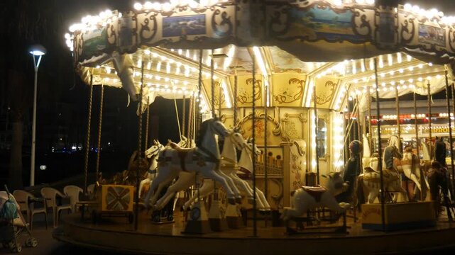 Handheld footage of a carousel turning around with ponies and with lights in the evening in city Frejus in France