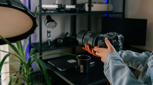 Hands holding a professional camera with a large lens in a creative studio setting