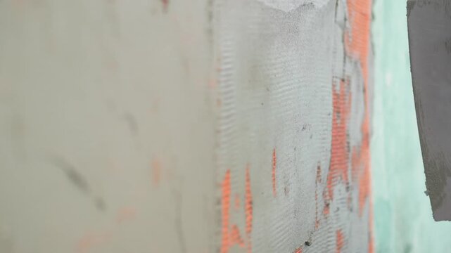 Construction worker applying cement plaster to exterior wall with trowel and mesh reinforcement