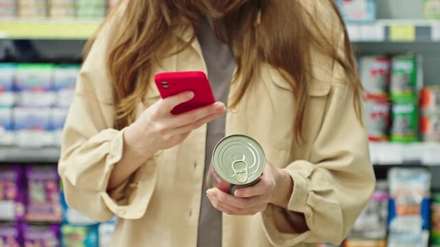 Woman Scanning Canned Pet Food Barcode With Smartphone In Supermarket, Using Mobile App To Check Product Information, Comparing Reviews And Price Before Purchase. Smart Shopping And Retail Concept.