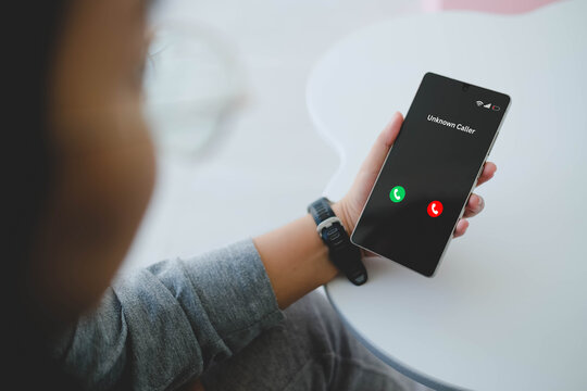 An over the shoulder view of a woman holding a smartphone displaying an incoming call screen from an unknown caller.