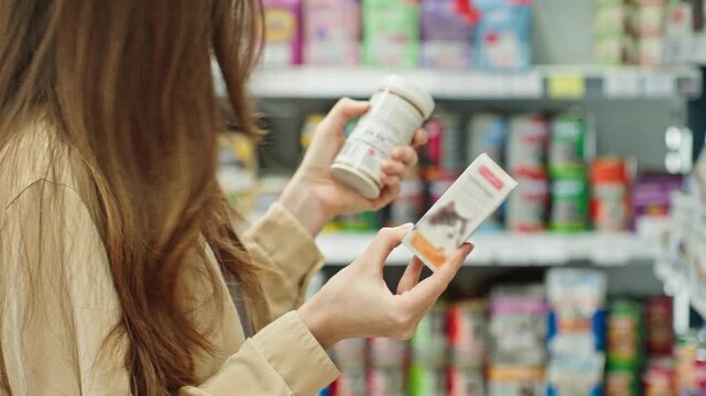 Woman Comparing Pet Vitamins And Reading Product Information In Store Before Purchase. Pet Care And Responsible Buying Decision Concept.