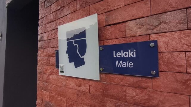 Clear signboards for a public Muslim prayer room are mounted on the wall. They feature male or female graphics with text in Malay and English. The signs are easily visible to the public.