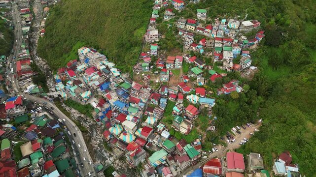 Panoramic aerial orbit of vibrant, colorful house rooftops along lush mountainside by a busy highway - Benguet, Philippines