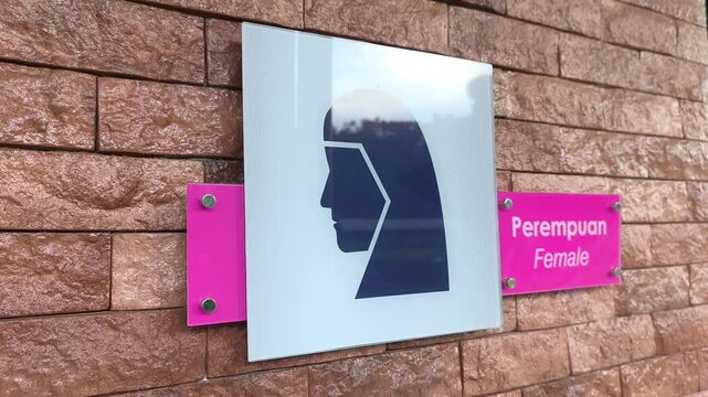 Clear signboards for a public Muslim prayer room are mounted on the wall. They feature male or female graphics with text in Malay and English. The signs are easily visible to the public.