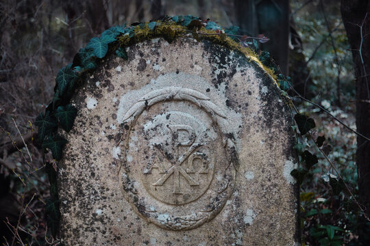 Ancient Stone Tombstone with Chi-Rho Symbol and Alpha Omega - Weathered Christian Grave in a Dark Misty Forest with Ivy