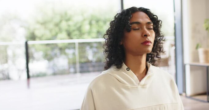 After sitting, non-binary adult inhaling holding breath then exhaling beside glass door and plant
