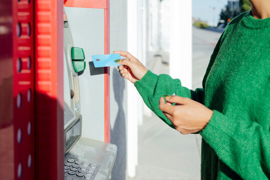 Hand inserting credit card into ATM for banking transaction outdoors
