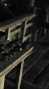 Workers organize tools, cups, and jugs on wooden tables in a rustic workshop. The scene shows preparation for crafts and daily activities in a busy work environment.