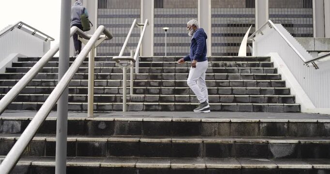 Mature African American man stretching leg on handrail at stairs mirroring runner ascent