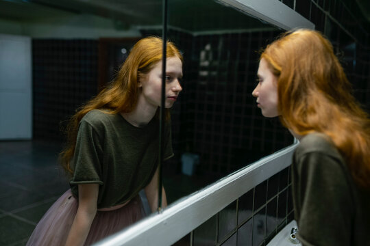 Red-haired woman with freckles reflecting in a mirror in an old building