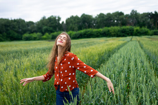 Smiling woman with curly hair in red blouse enjoying summer in wheat field