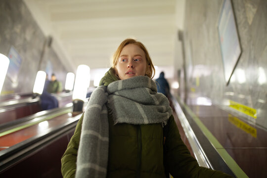 Red-haired woman with scarf on subway escalator indoors