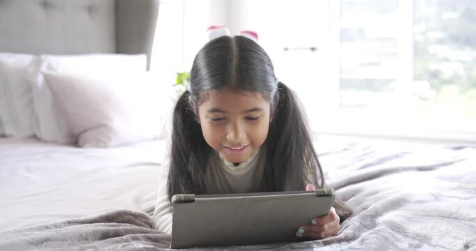 As scene is starting, child is tapping and swiping tablet on bed, smiling and laughing, refocusing