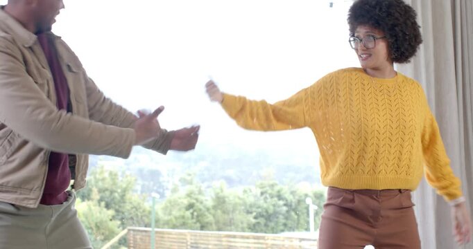 African American couple exchanging playful glance and dancing beside wooden table at window for fun