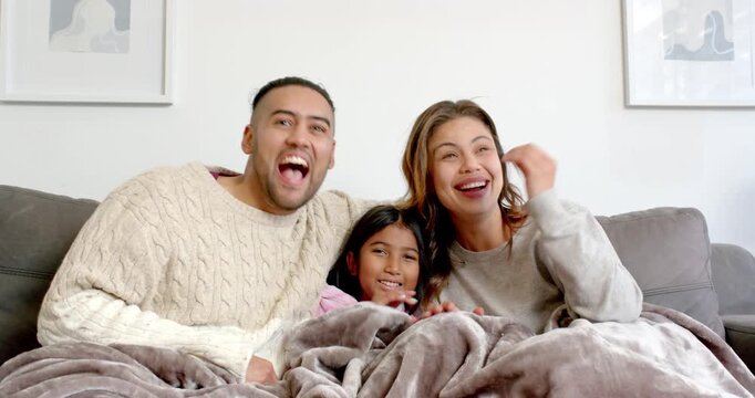 Family of three reacting to off-screen stimulus by laughing, pointing under blanket on sofa at home