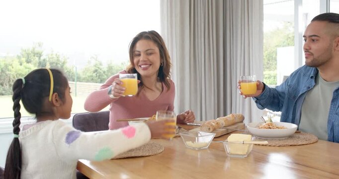 Family of three starting meal at home, breaking bread, twirling pasta, toasting glasses sharing joy