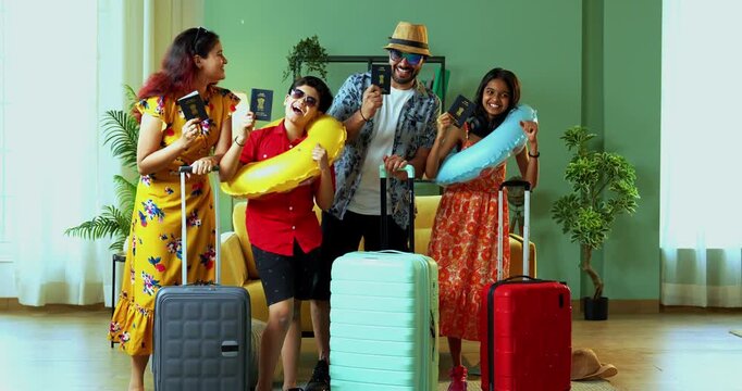 Happy young Indian family in vacation attire standing in a modern home, flaunting passports and suitcases. Cheerful parents and kids ready for an international holiday trip