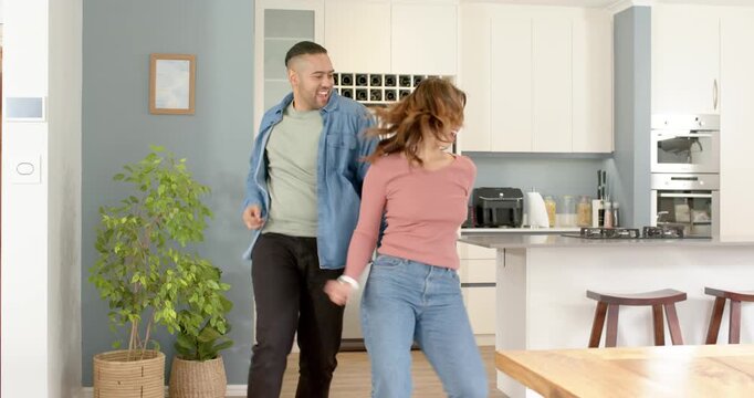 Couple stepping into view in kitchen performing hip sways toward counter and refrigerator for fun